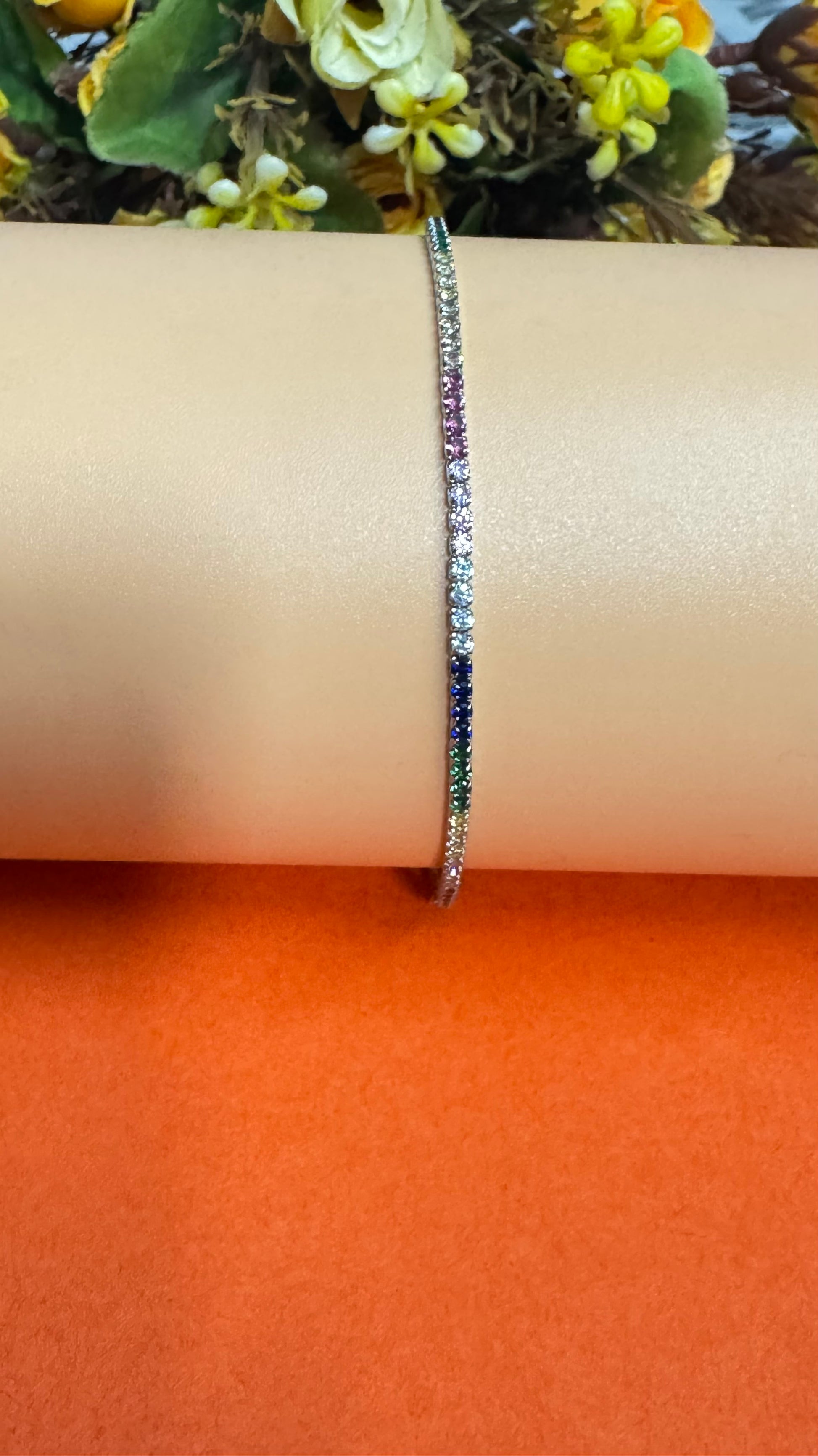 Bracelet with multicolored stones on a wrist against an orange background
