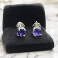 Pair of purple gemstone earrings on a black cushion with a blurred background