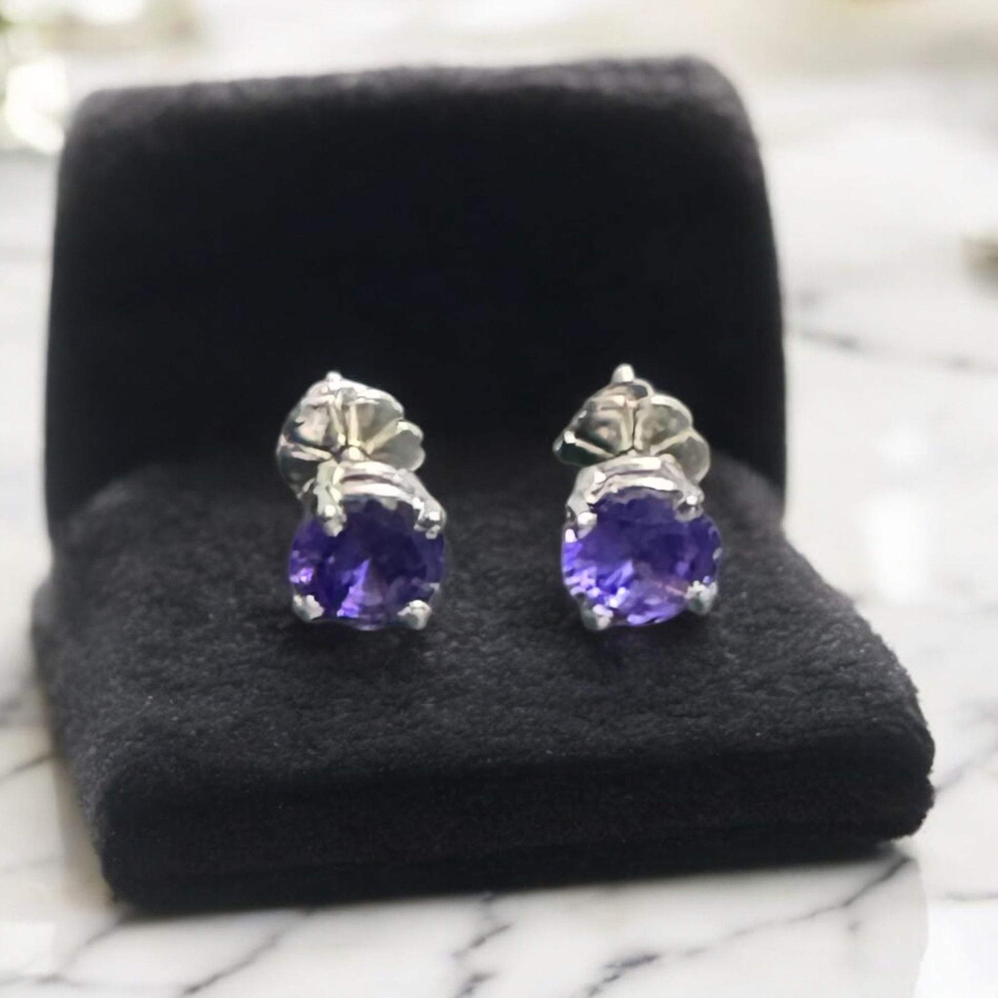 Pair of purple gemstone earrings on a black cushion with a blurred background