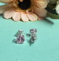 Silver earrings with pink gemstones on a light blue surface with flowers in the background