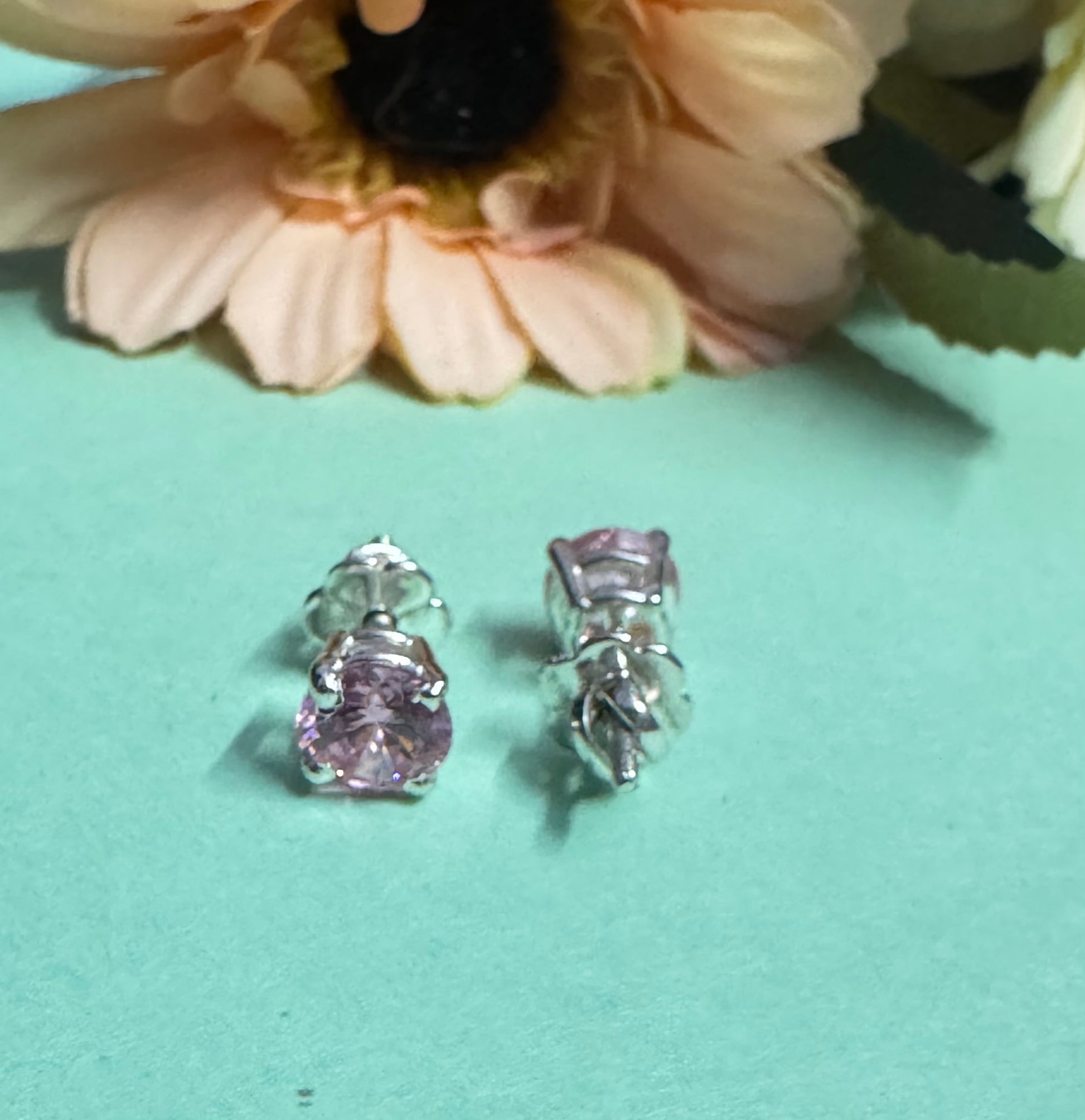 Silver earrings with pink gemstones on a light blue surface with flowers in the background