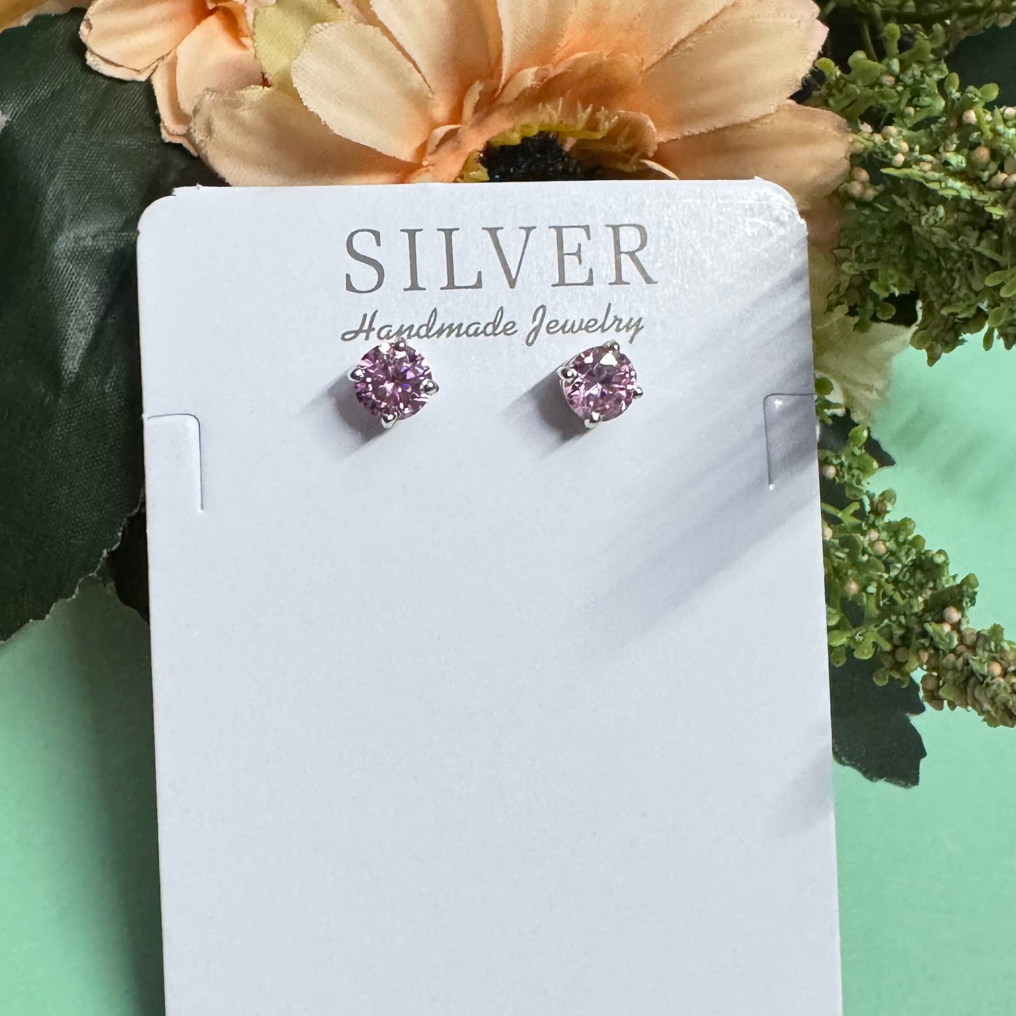 Silver earrings on a card with 'SILVER Handmade Jewelry' text, surrounded by flowers.