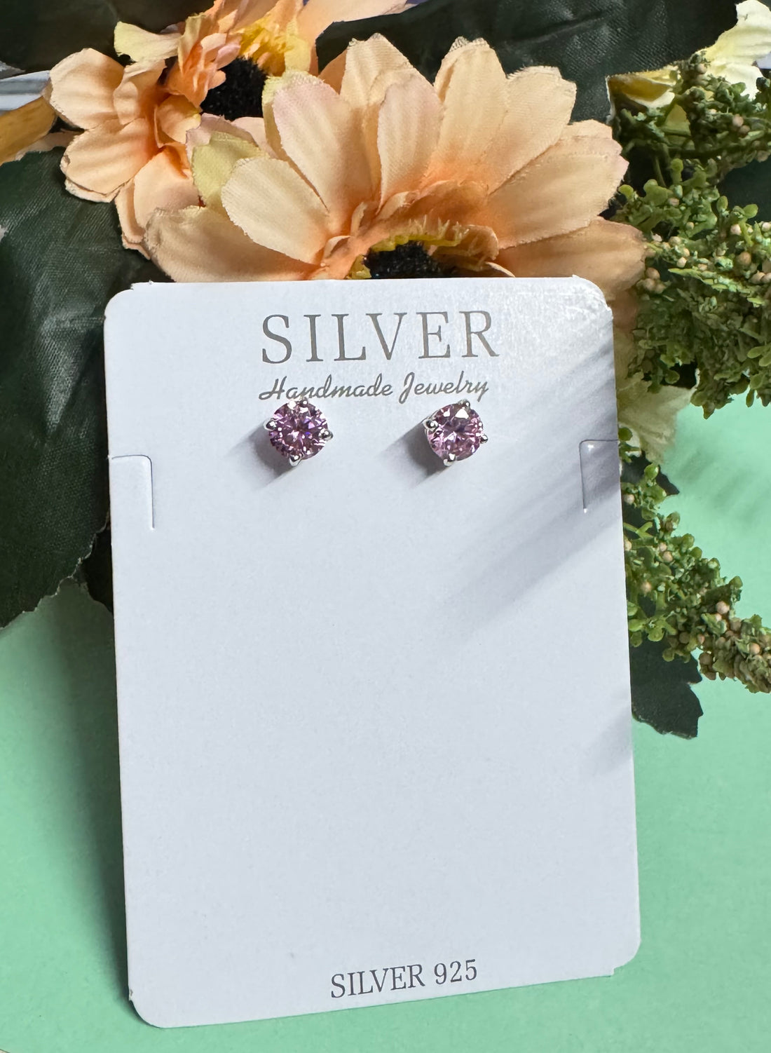Silver earrings on a card with 'SILVER Handmade Jewelry' text, surrounded by flowers.