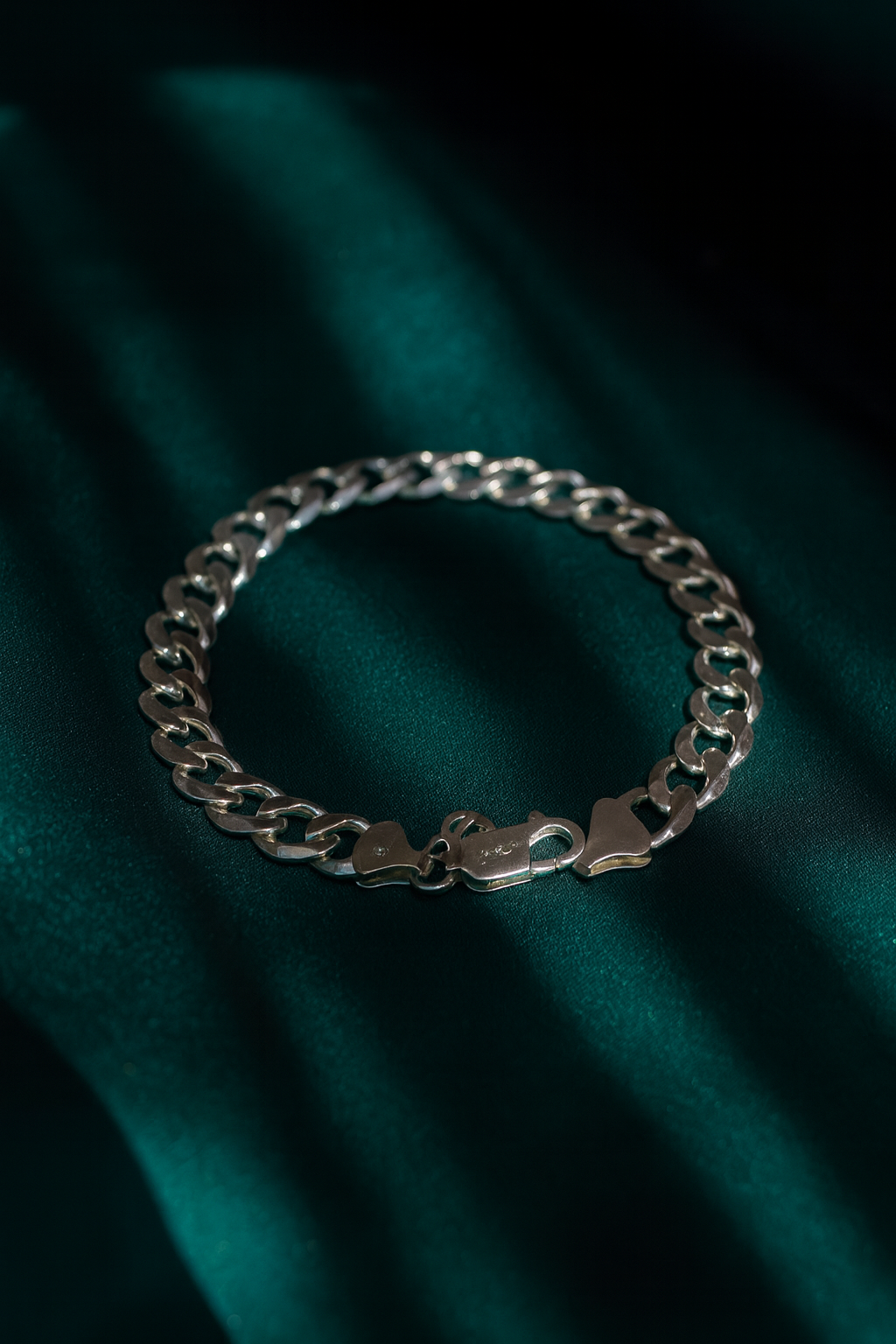Silver chain bracelet on a black stand with flowers in the background