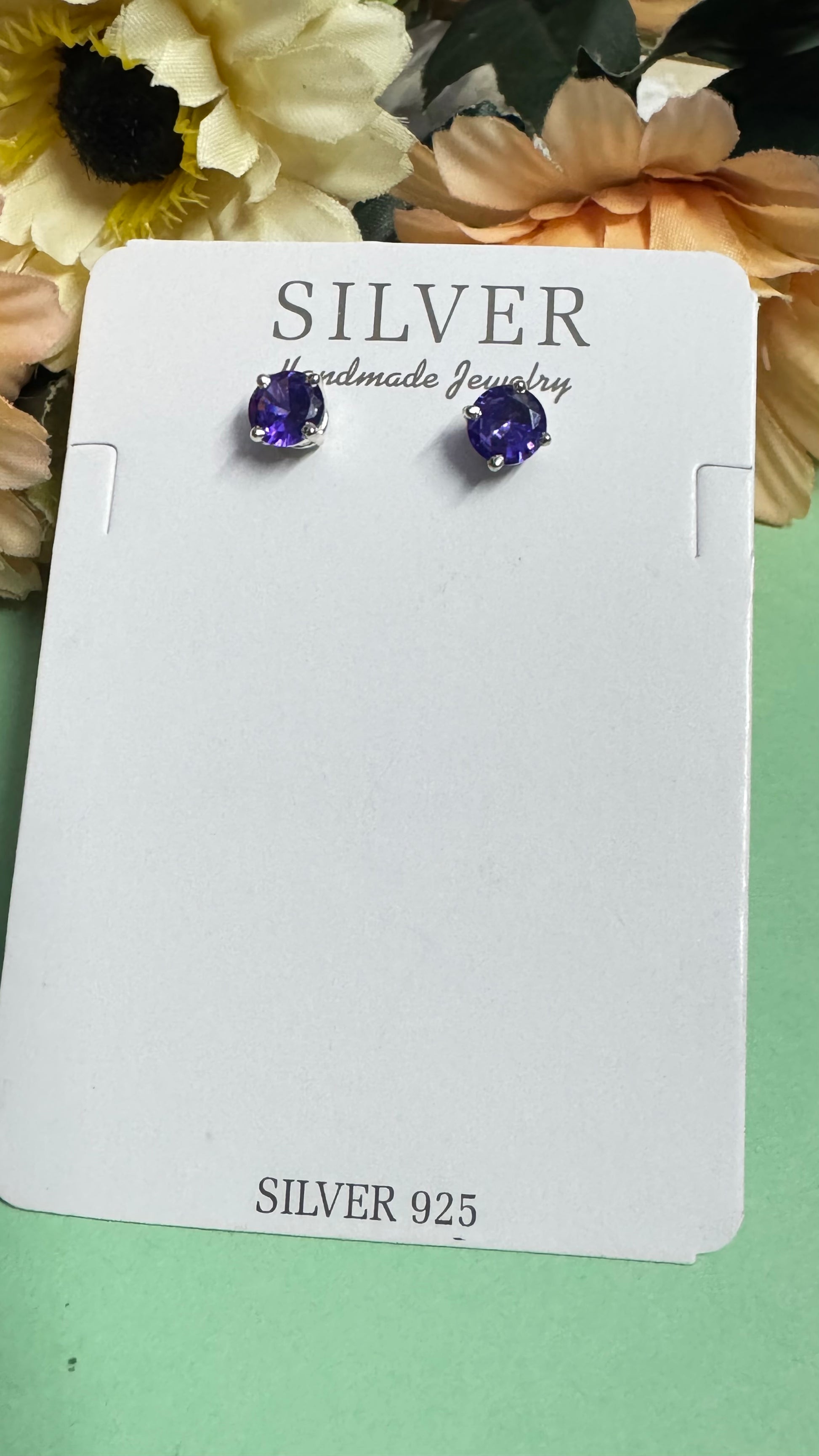 Silver earrings with purple gemstones on a branded card against a floral background