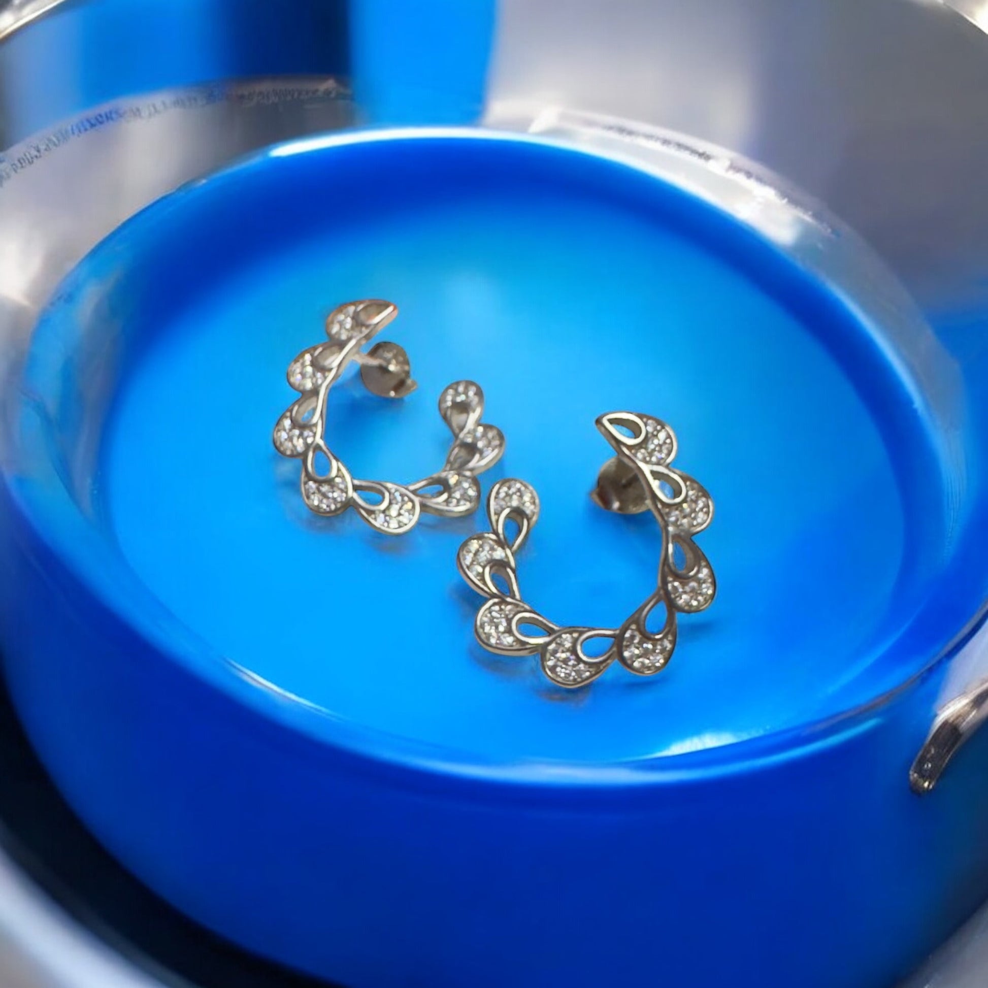 Pair of gold hoop earrings with clear stones on a blue dish