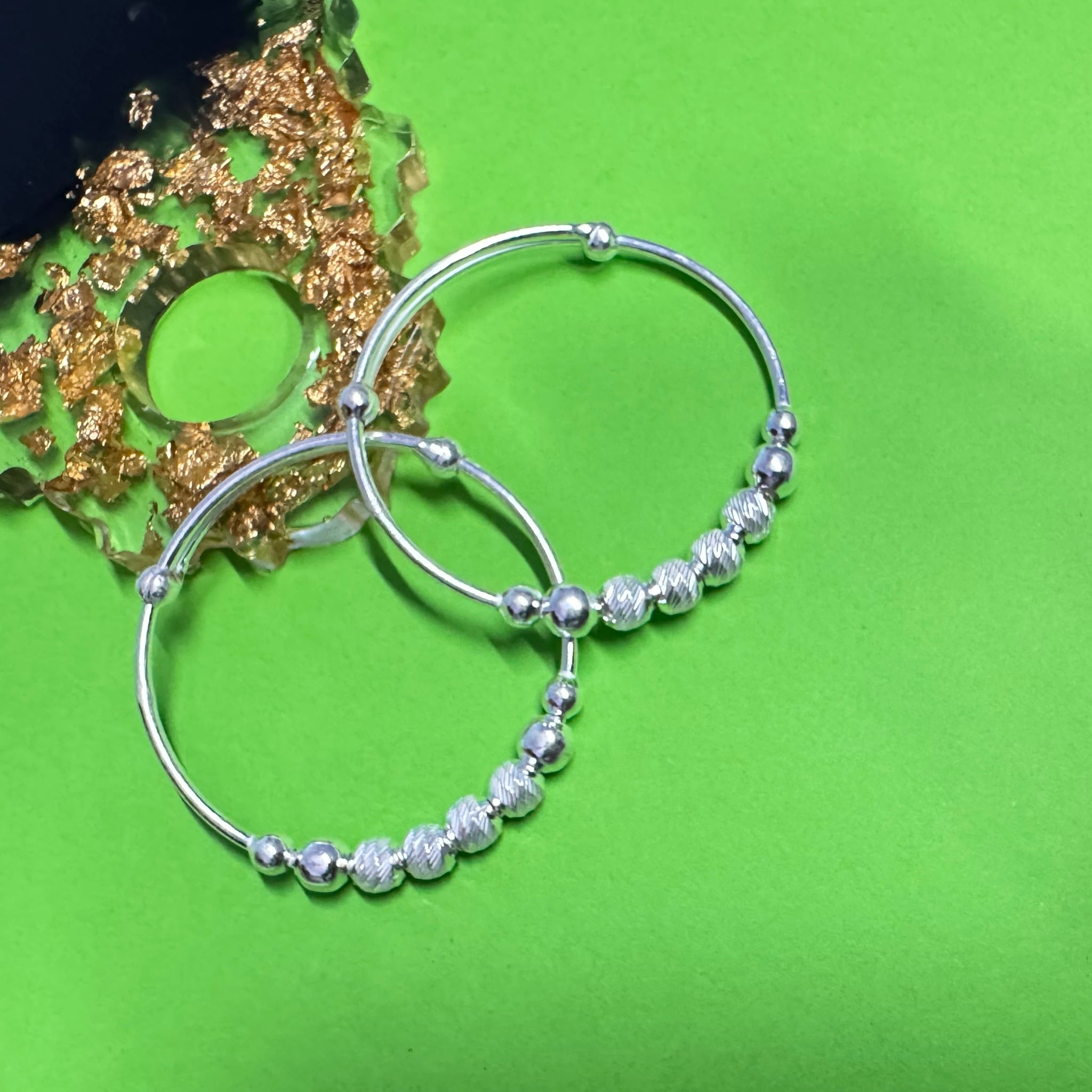 Silver hoop earrings with bead detailing on a green background