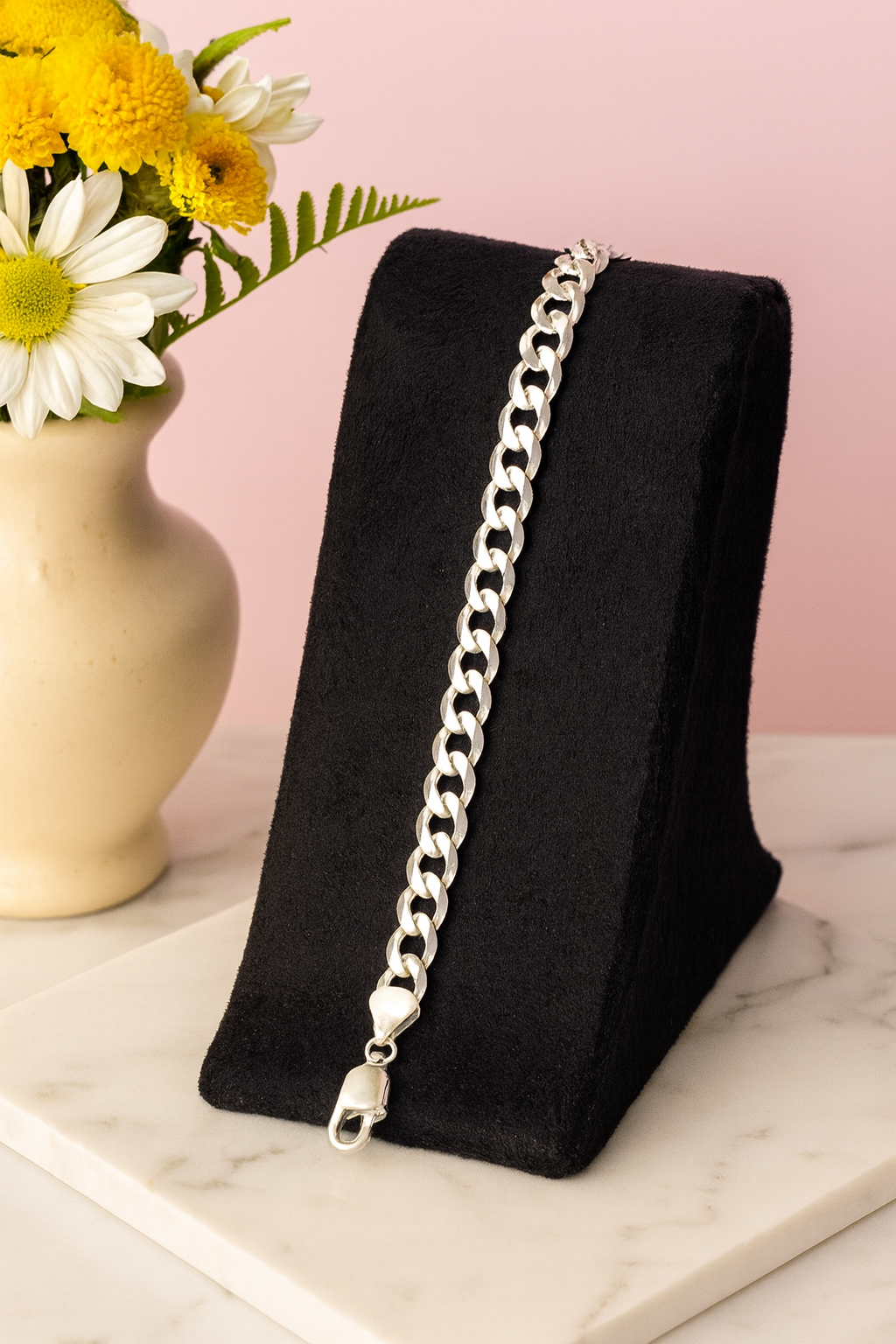 Silver chain bracelet on a black stand with flowers in the background