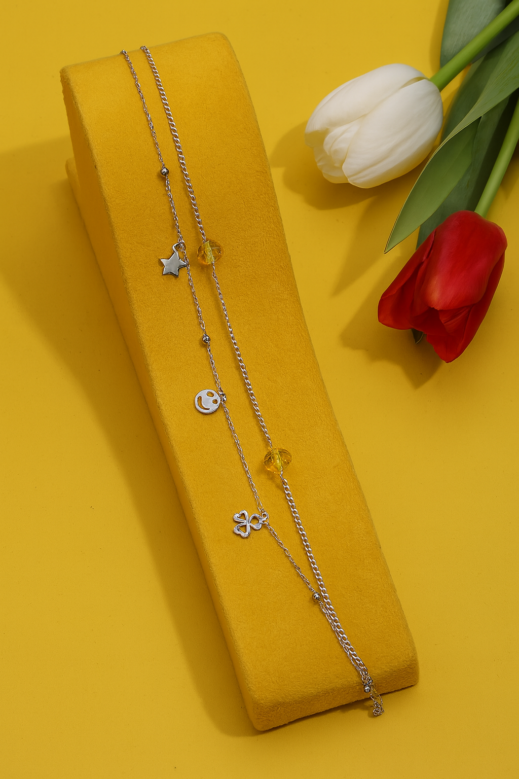 Sterling silver charm anklet with star, smiley, and heart pendants on yellow background
