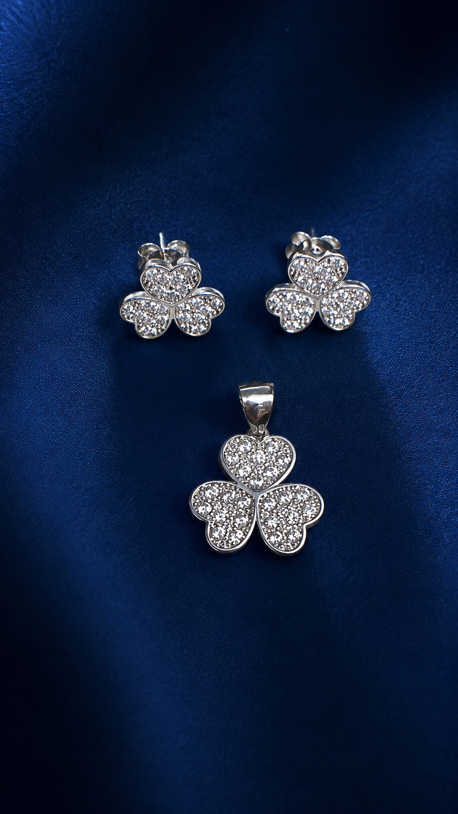 A silver-toned jewelry set featuring a four-leaf clover pendant and matching stud earrings