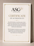 A vertical Certificate of Authenticity card from ASG Silver House, featuring gold decorative borders and text on an off-white background, photographed against a neutral beige backdrop.