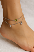 Ankle with multiple silver anklets featuring star charms on a neutral background