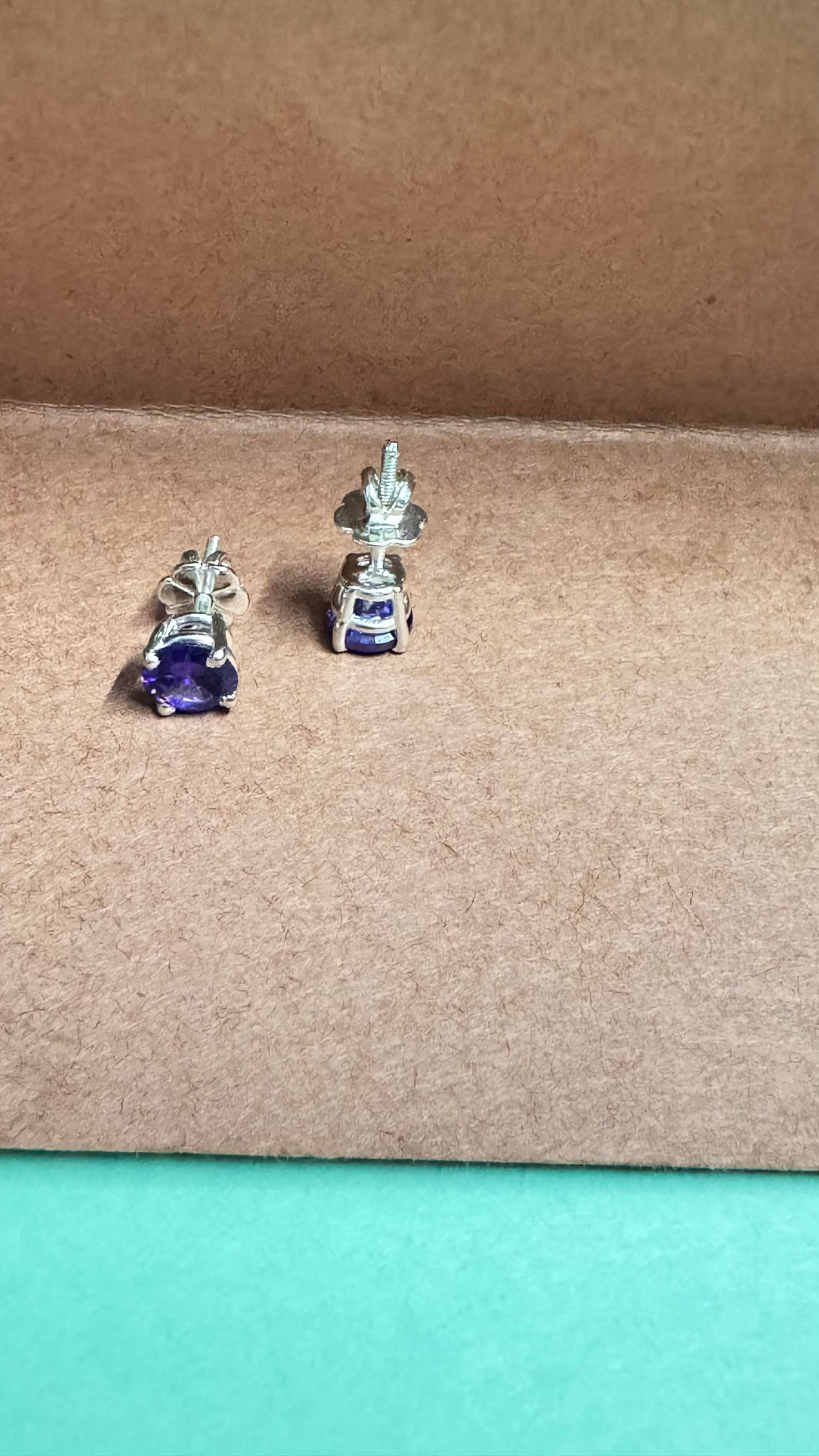 Pair of blue gemstone stud earrings on a brown card with flowers in the background.
