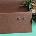 Pair of purple gemstone earrings on a brown card with flowers in the background