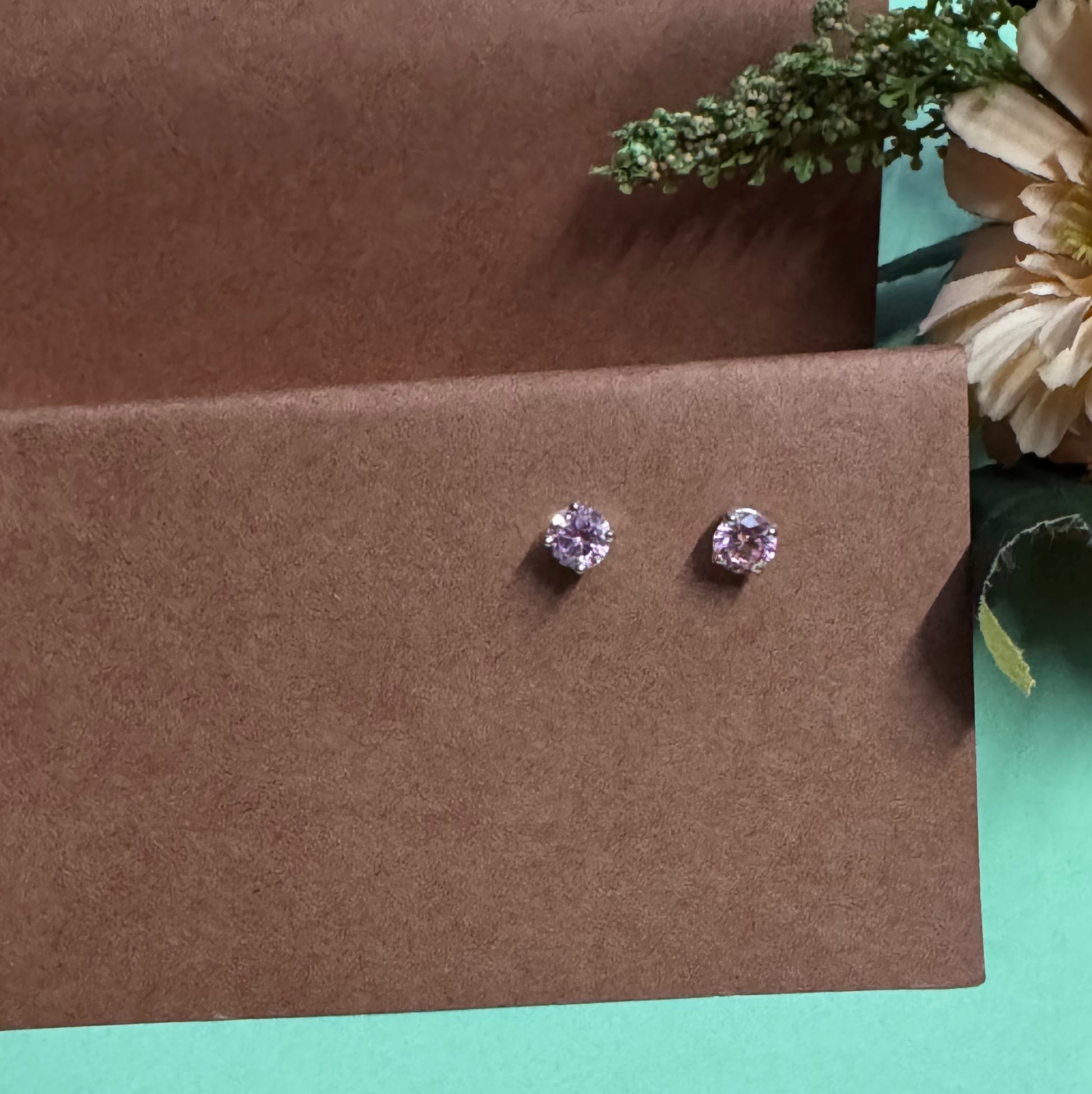 Pair of purple gemstone earrings on a brown card with flowers in the background