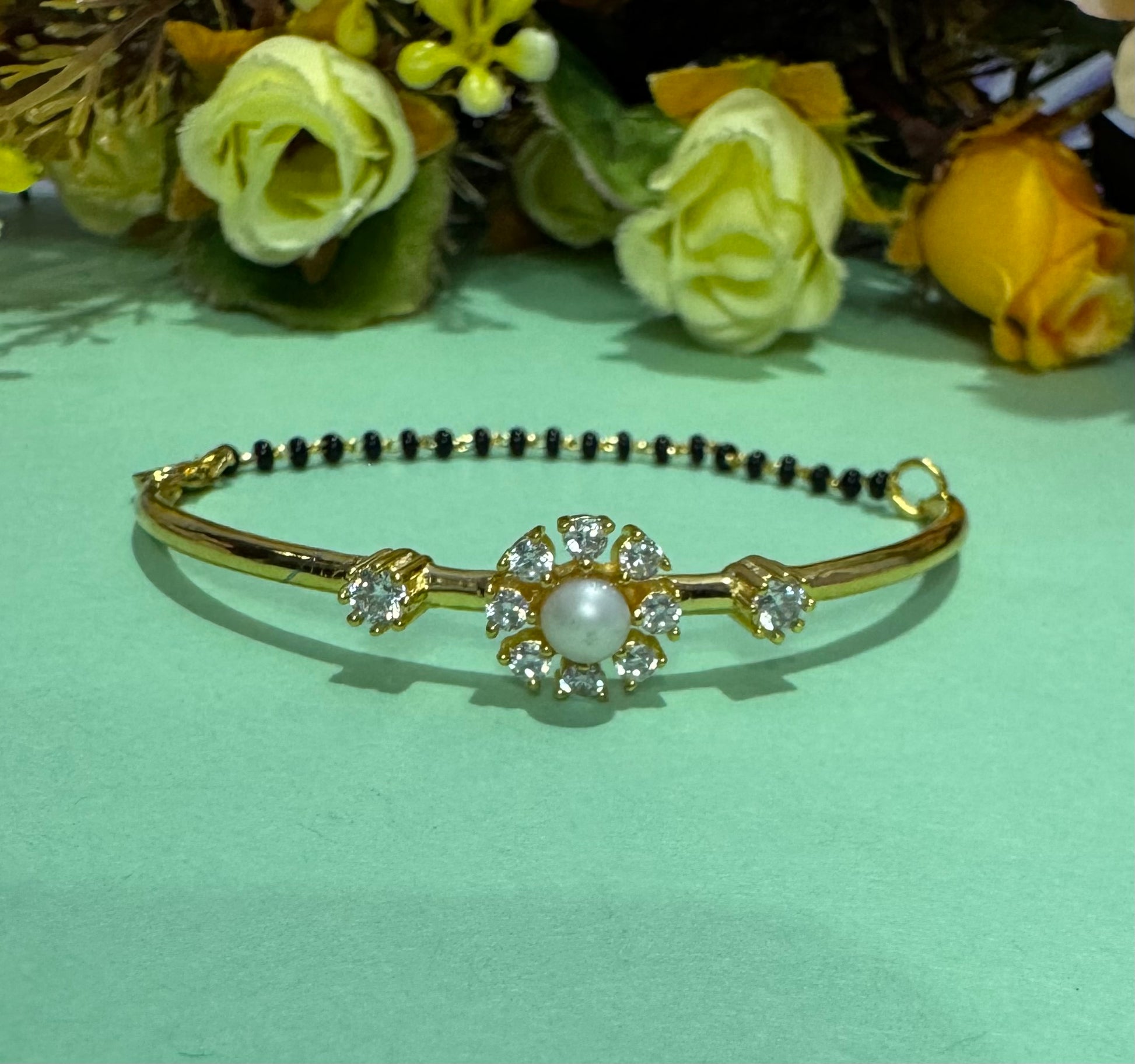 Gold bracelet with pearl and gemstone design on a light green background