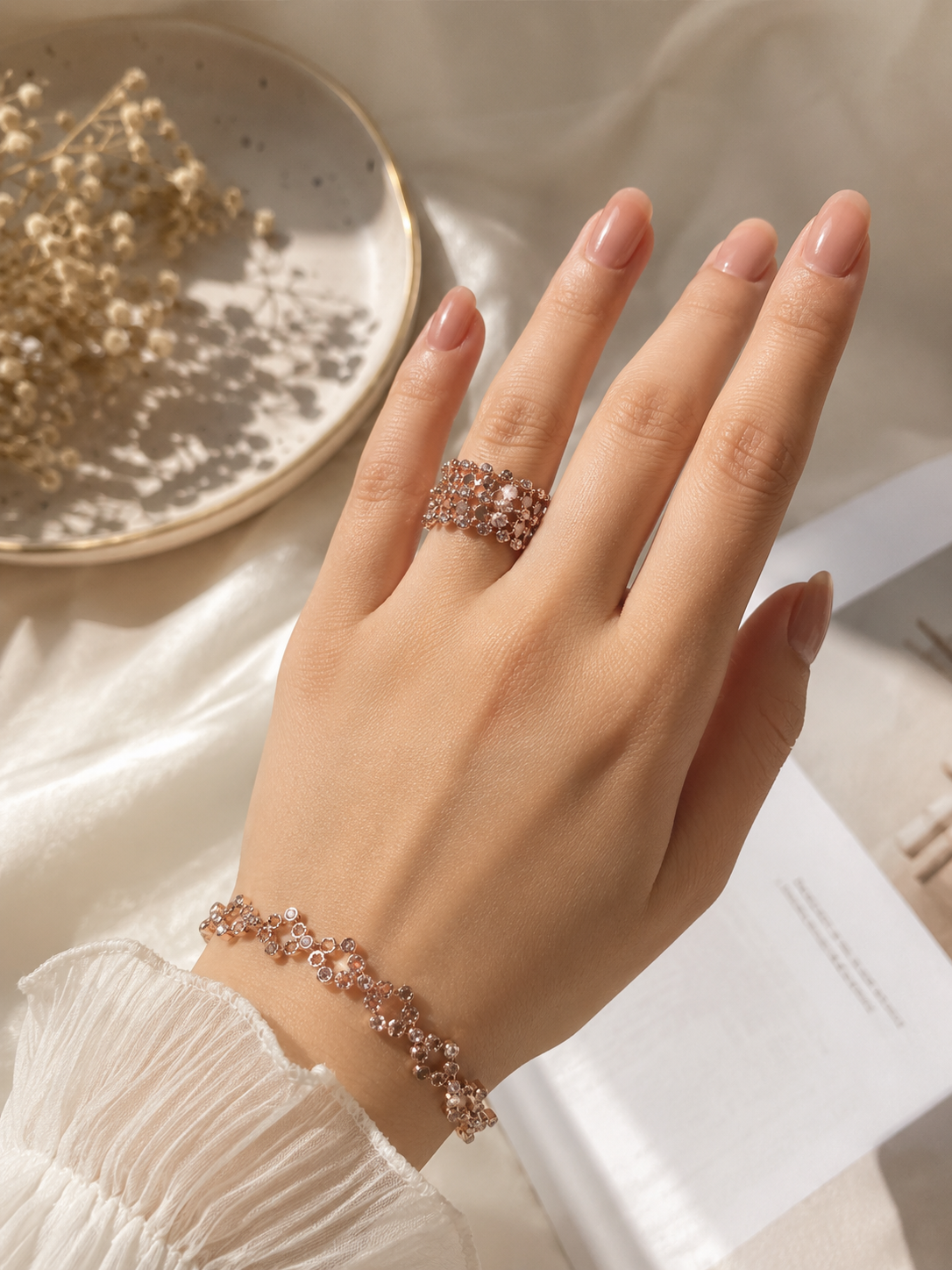 Hand wearing a rose gold bracelet and ring on a neutral background