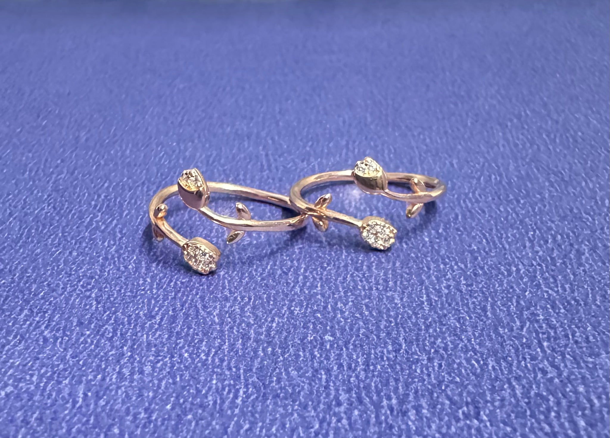 Pair of gold earrings with floral designs on a blue textured background
