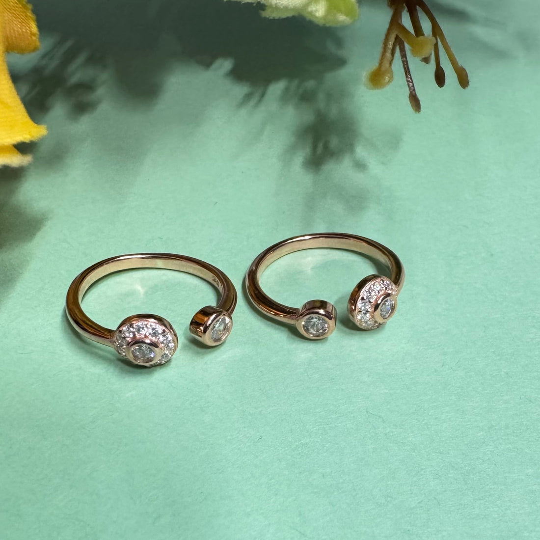 Two rose gold rings with gemstones on a light green background