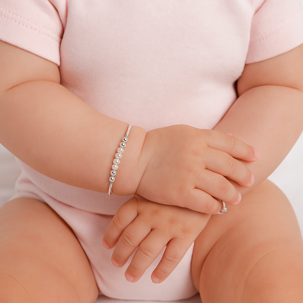 Baby wearing a silver bracelet with pearls on a plain background