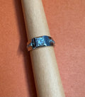 Silver ring with a large diamond on a wooden dowel against a pink background