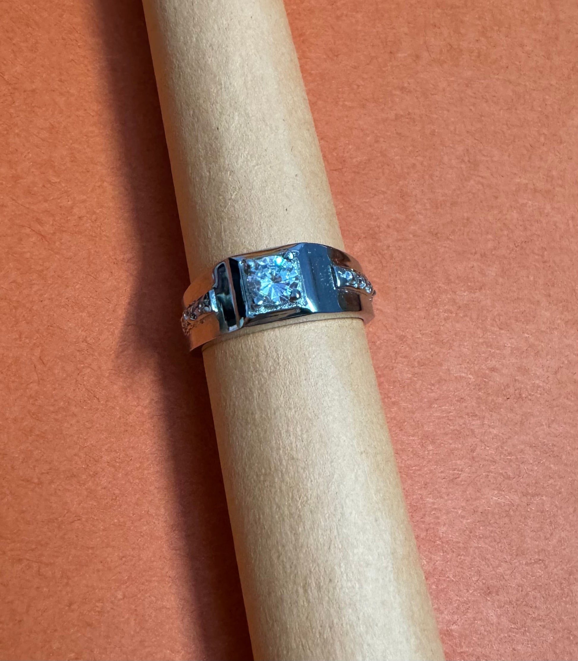 Silver ring with a large diamond on a wooden dowel against a pink background