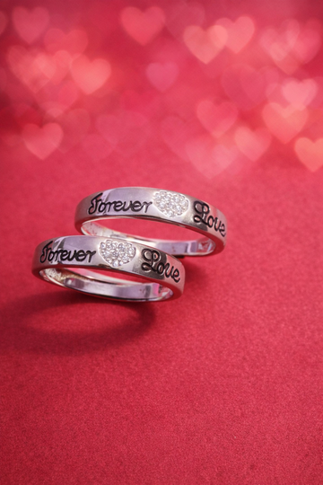 Two silver rings with 'Forever Love' engraving on a red background with heart shapes.