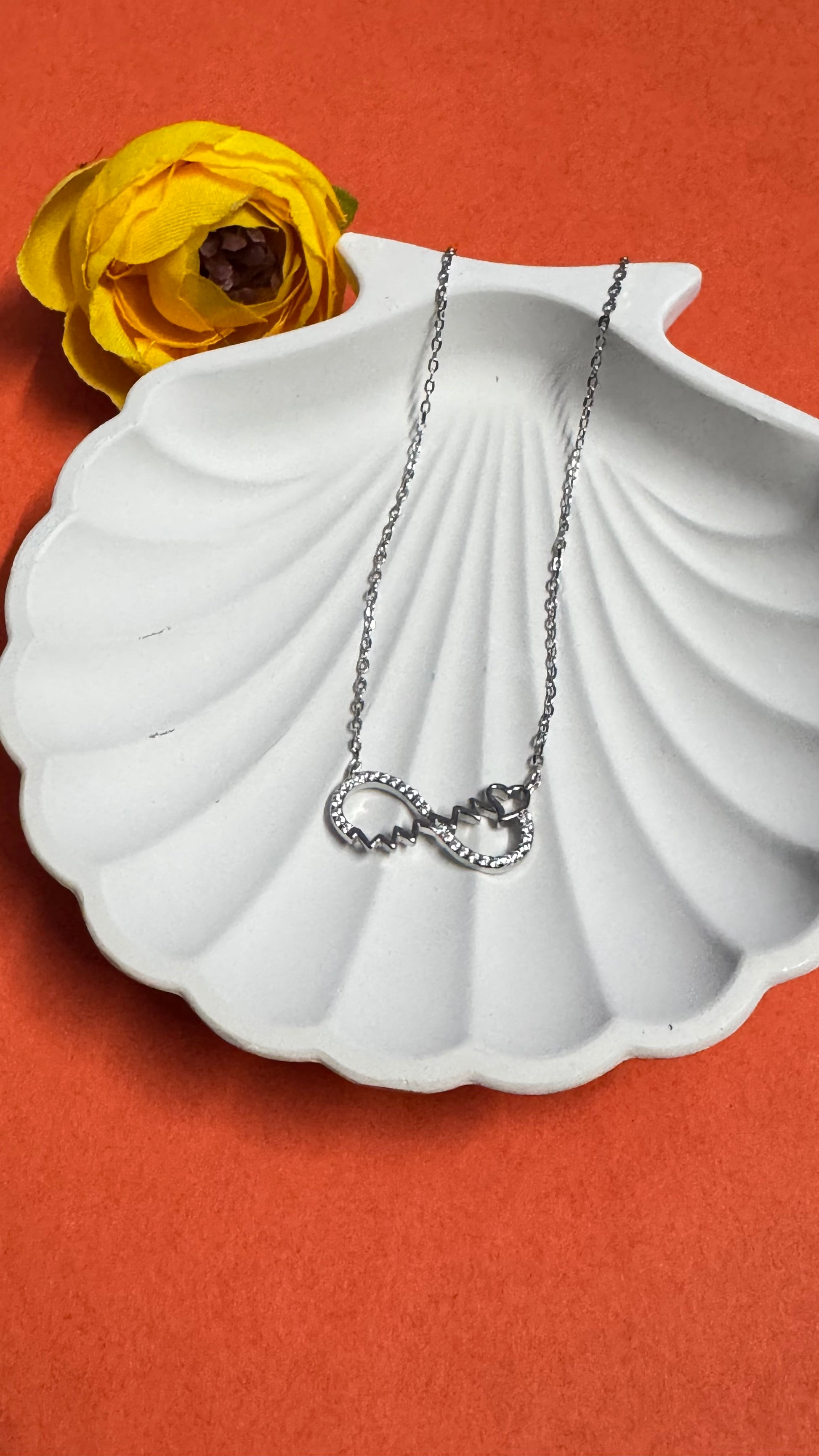 Silver necklace with a heart pendant on a white shell-shaped dish against an orange background