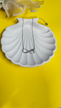 Necklace with a heart pendant on a white shell-shaped stand against a yellow background