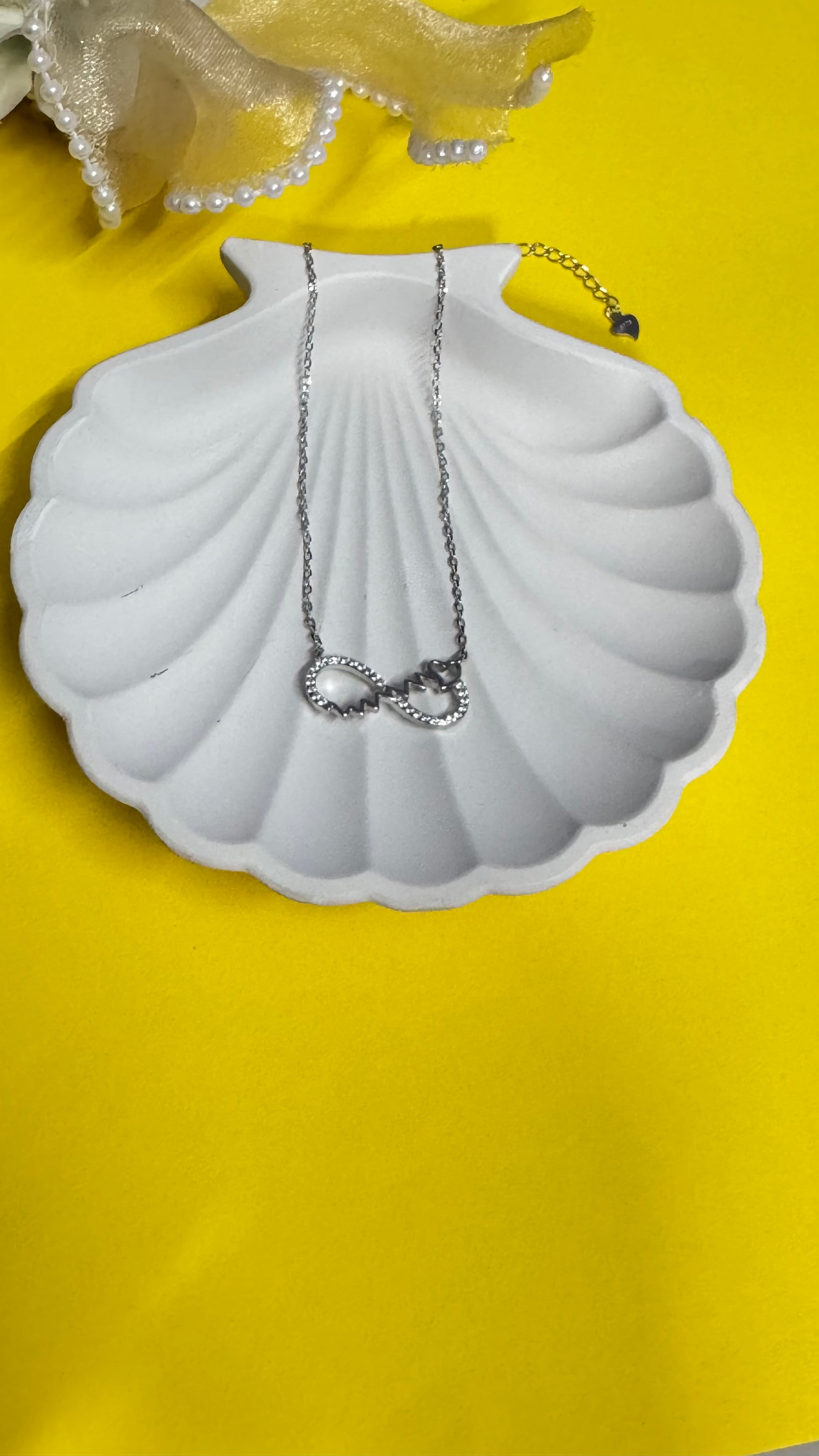 Necklace with a heart pendant on a white shell-shaped stand against a yellow background