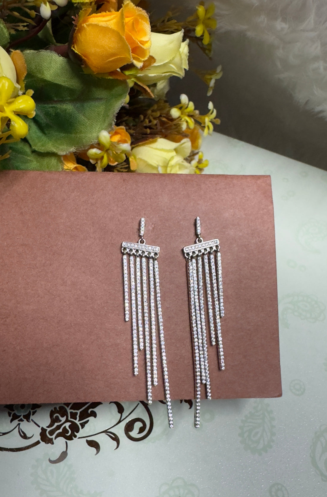 Silver fringe earrings on a black surface with green leaves in the background