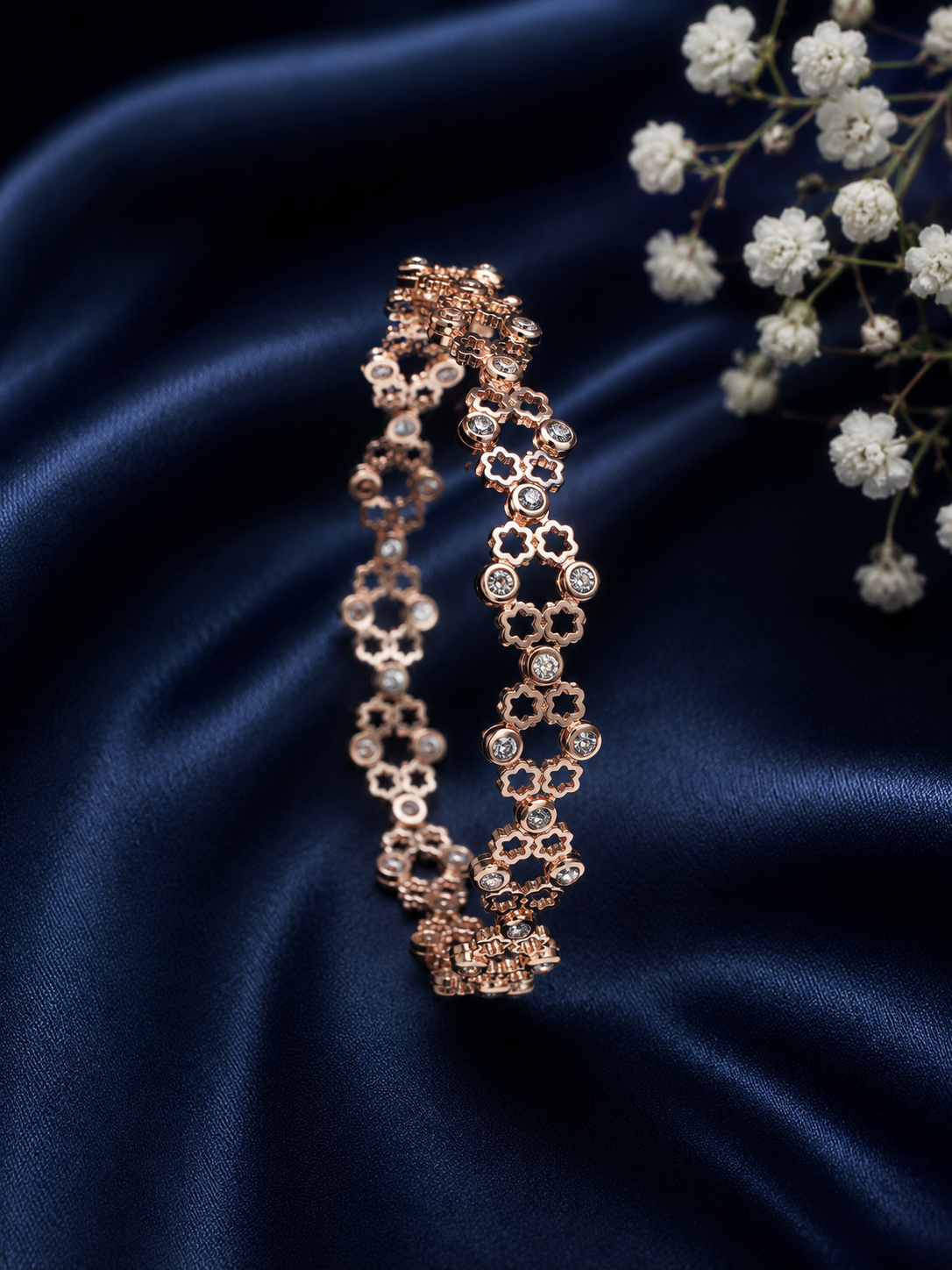 Luxury rose gold bracelet flat lay with navy blue satin and white flowers