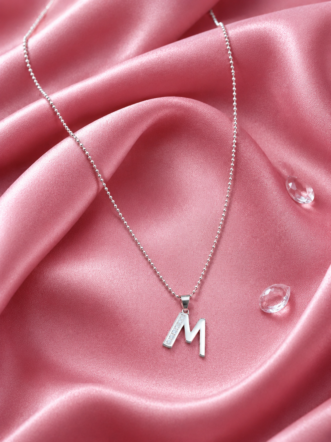 Silver necklace with a 'M' pendant on a pink fabric background