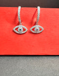 Pair of silver eye-shaped earrings with gemstones on a red surface