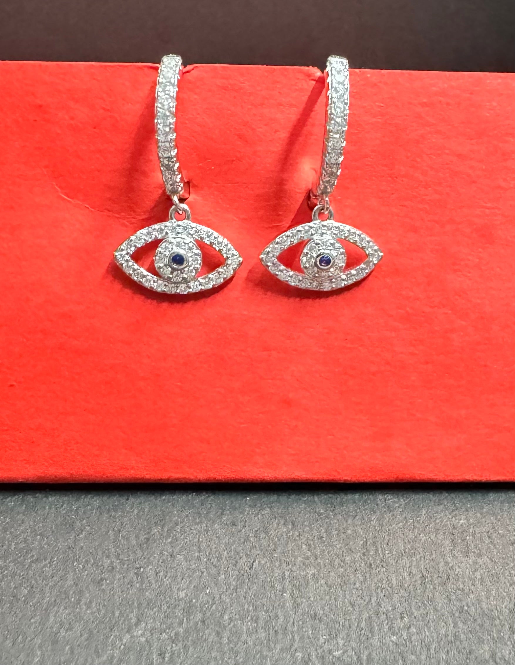 Pair of silver eye-shaped earrings with gemstones on a red surface