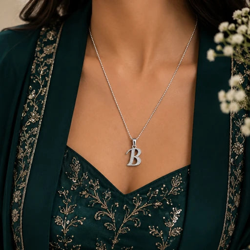 Person wearing a silver necklace with a 'B' pendant against a neutral background