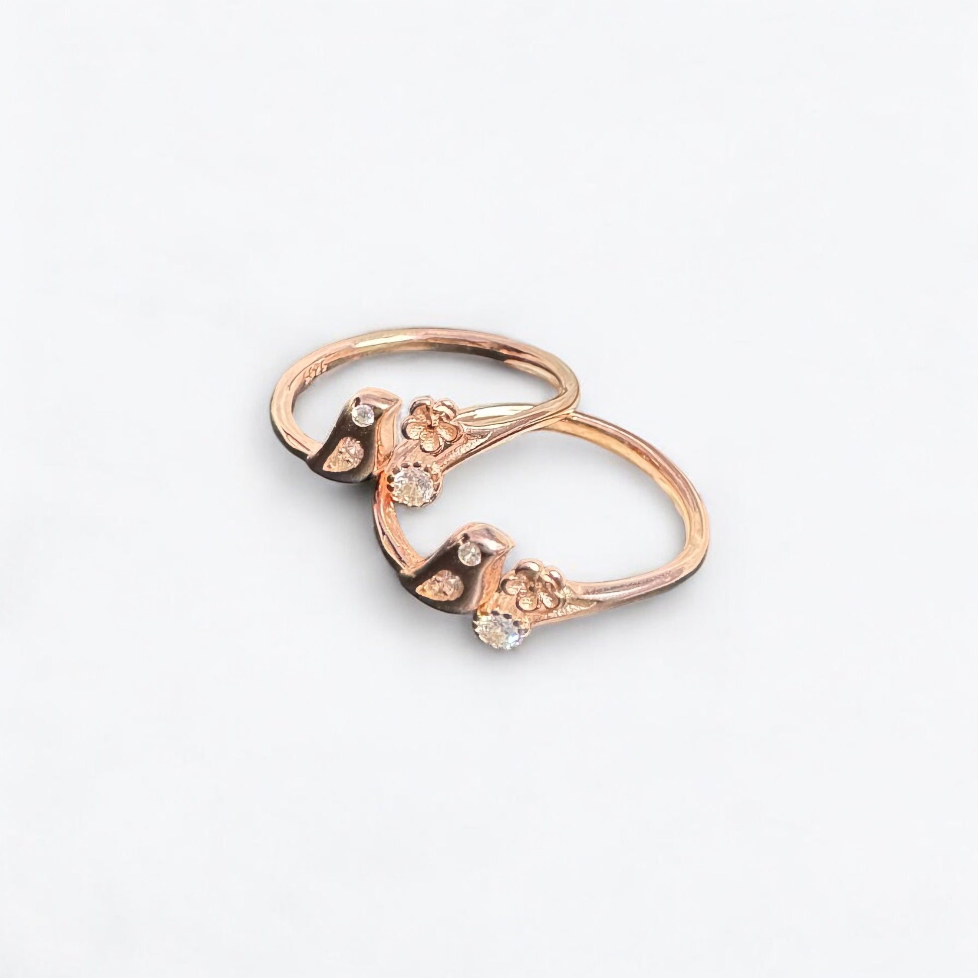 Rose gold ring with floral design and small diamonds on a light gray background