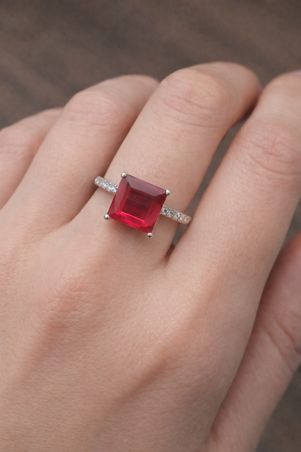 Ring with a red gemstone on a finger against a neutral background