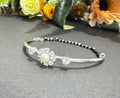 Silver bracelet with pearl accents on a gray surface with flowers in the background