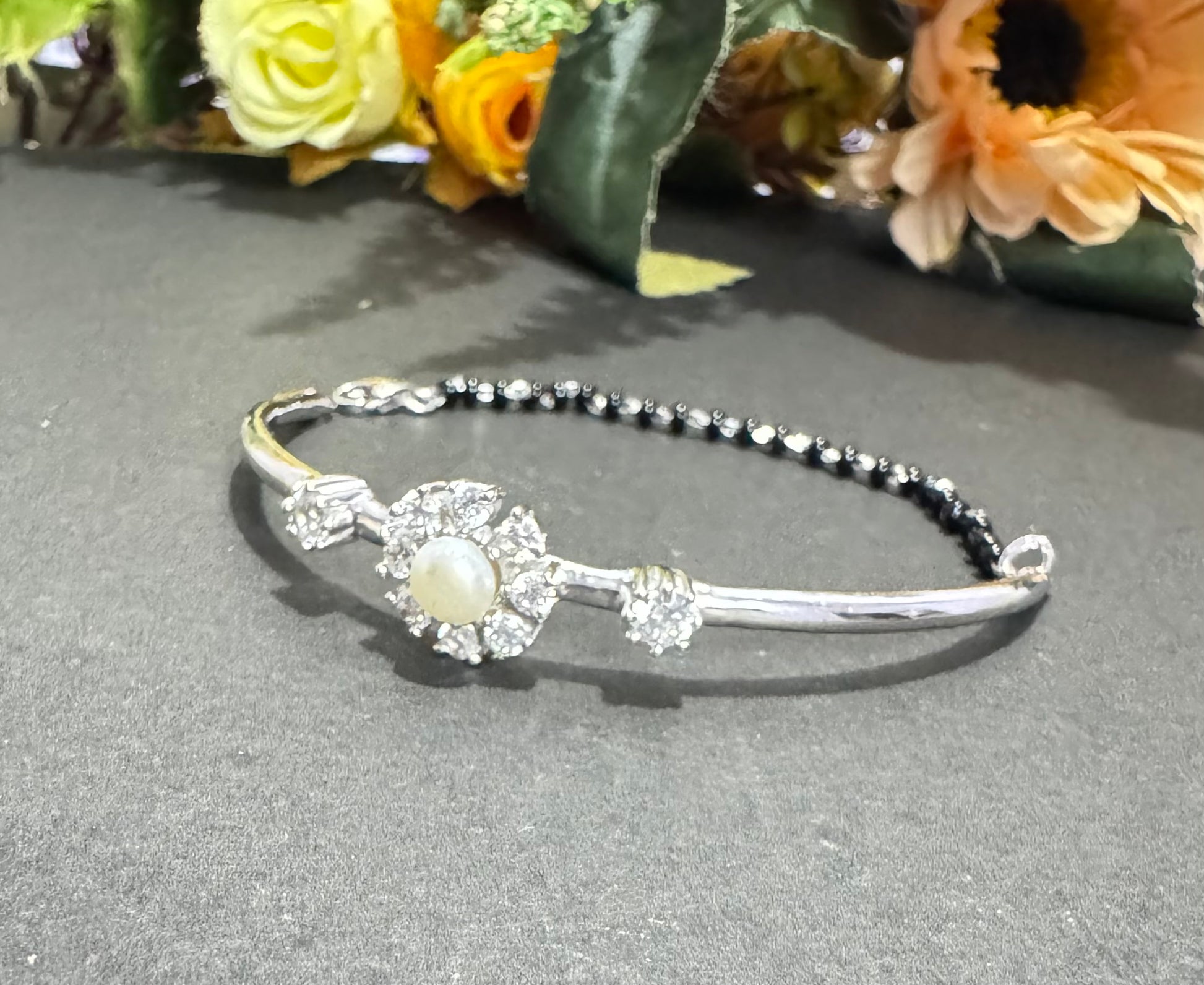 Silver bracelet with pearl accents on a gray surface with flowers in the background