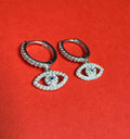 Silver hoop earrings with eye-shaped charms on a red background