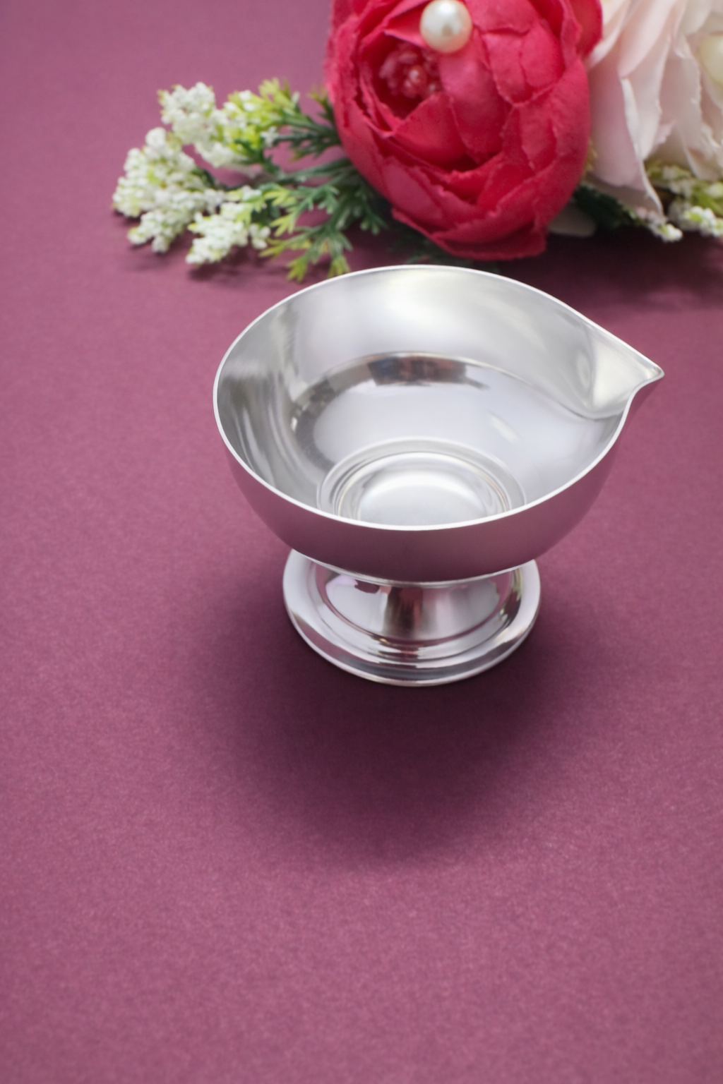 Silver ladle on a purple surface with flowers in the background