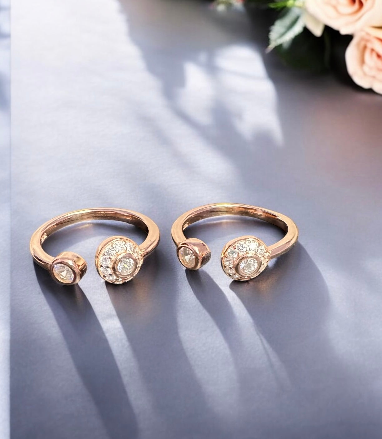 Pair of rose gold rings with gemstones on a reflective surface