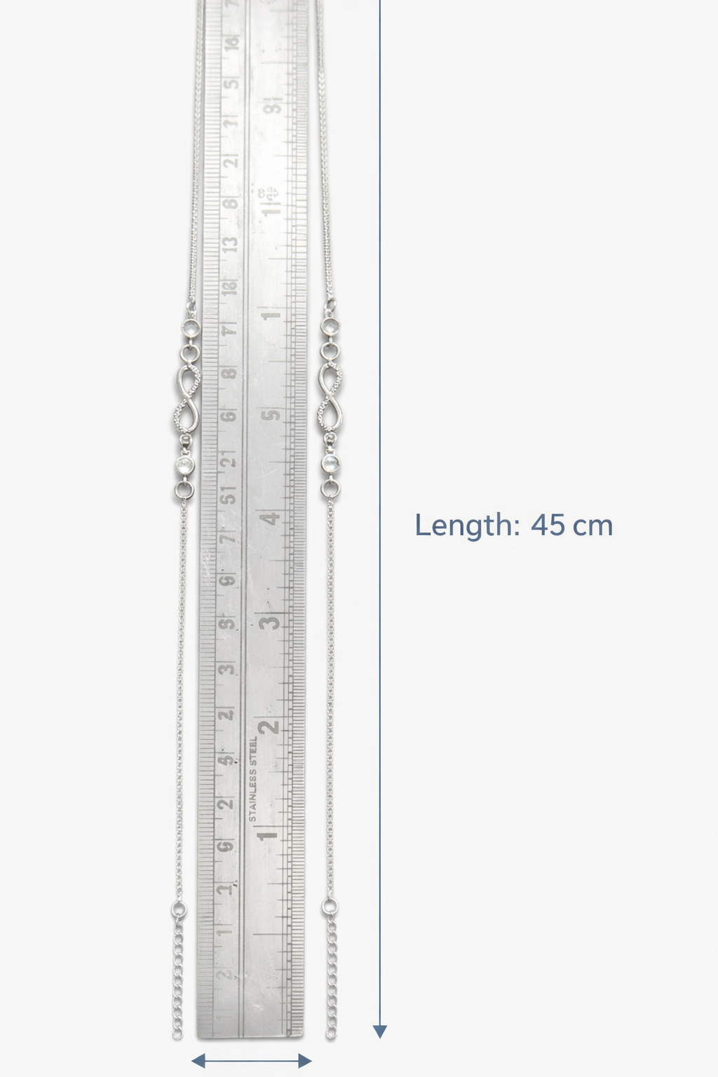 Silver anklets with a ruler for scale on a white background