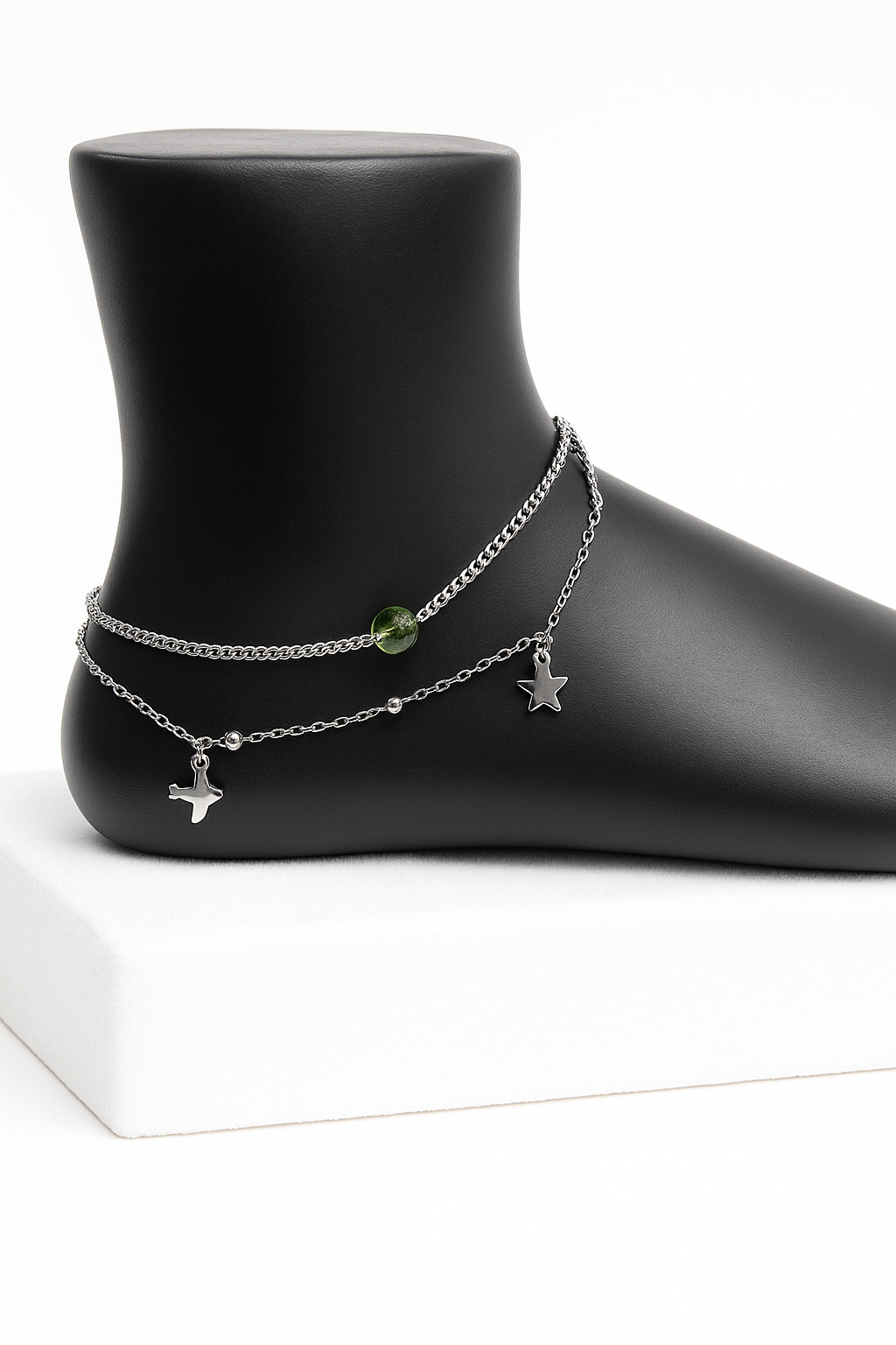 Ankle bracelet with charms on a black mannequin foot against a white background