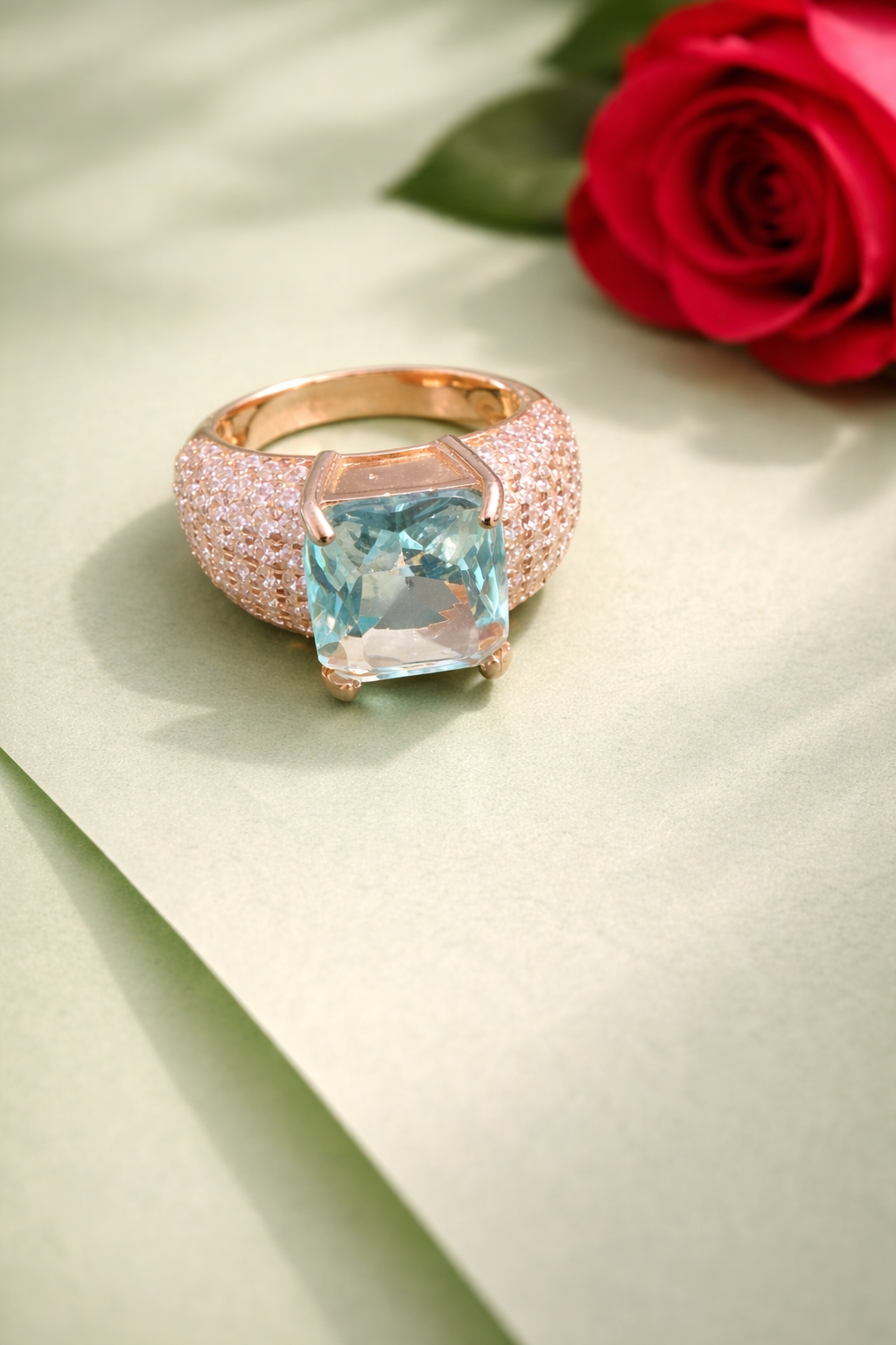 Rose gold ring with a blue gemstone next to a red rose on a light green background