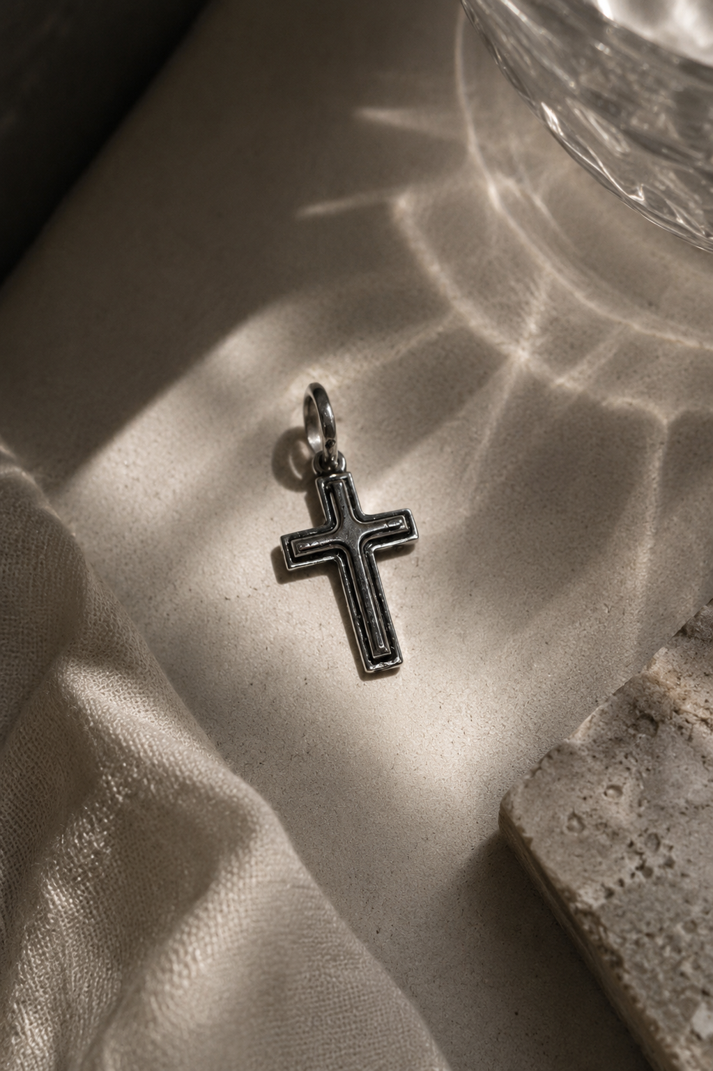 Silver cross pendant on a textured surface with sunlight casting shadows