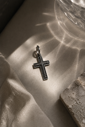 Silver cross pendant on a textured surface with sunlight casting shadows