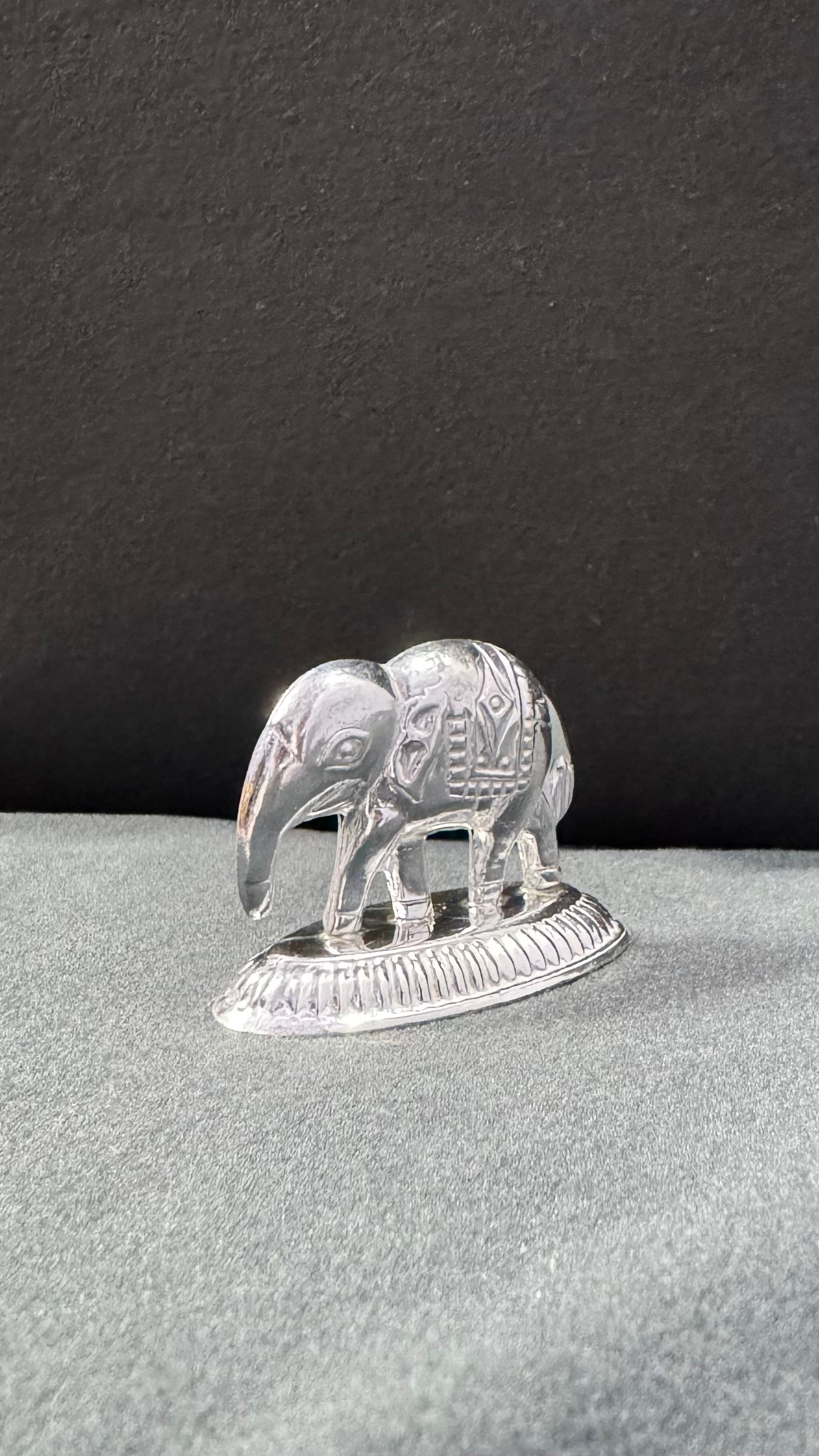 Silver elephant figurine on a gray surface with a black background