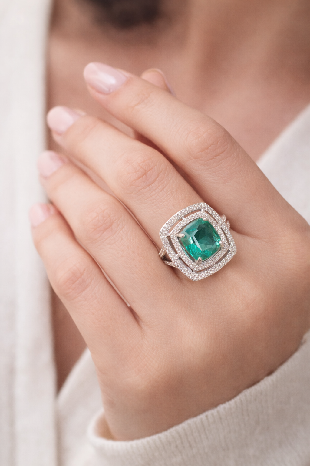 Emerald ring with diamond accents on a black book with blurred lights and flowers in the background